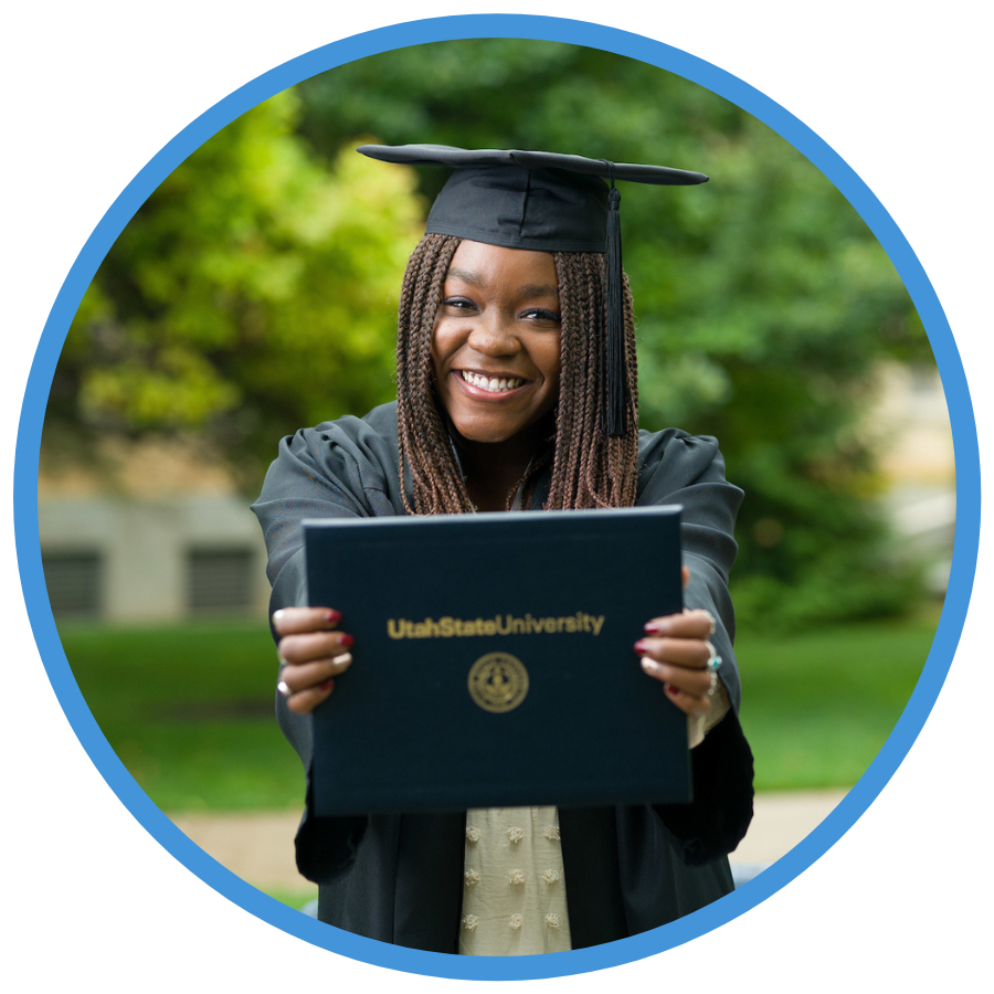 USU student in cap and gown smiling holding degree cover.