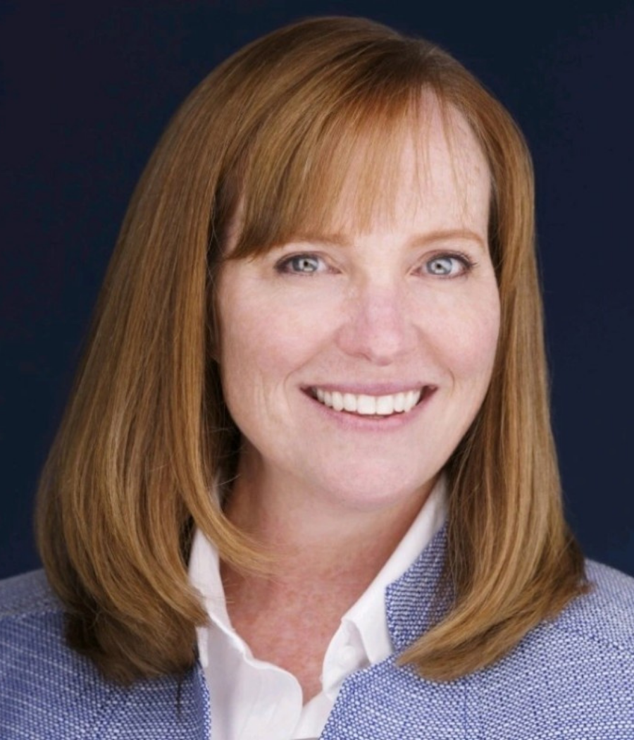 Jill Anderson, a woman with red hair and bangs wearing a white shirt and dark blazer, smiling at the camera.