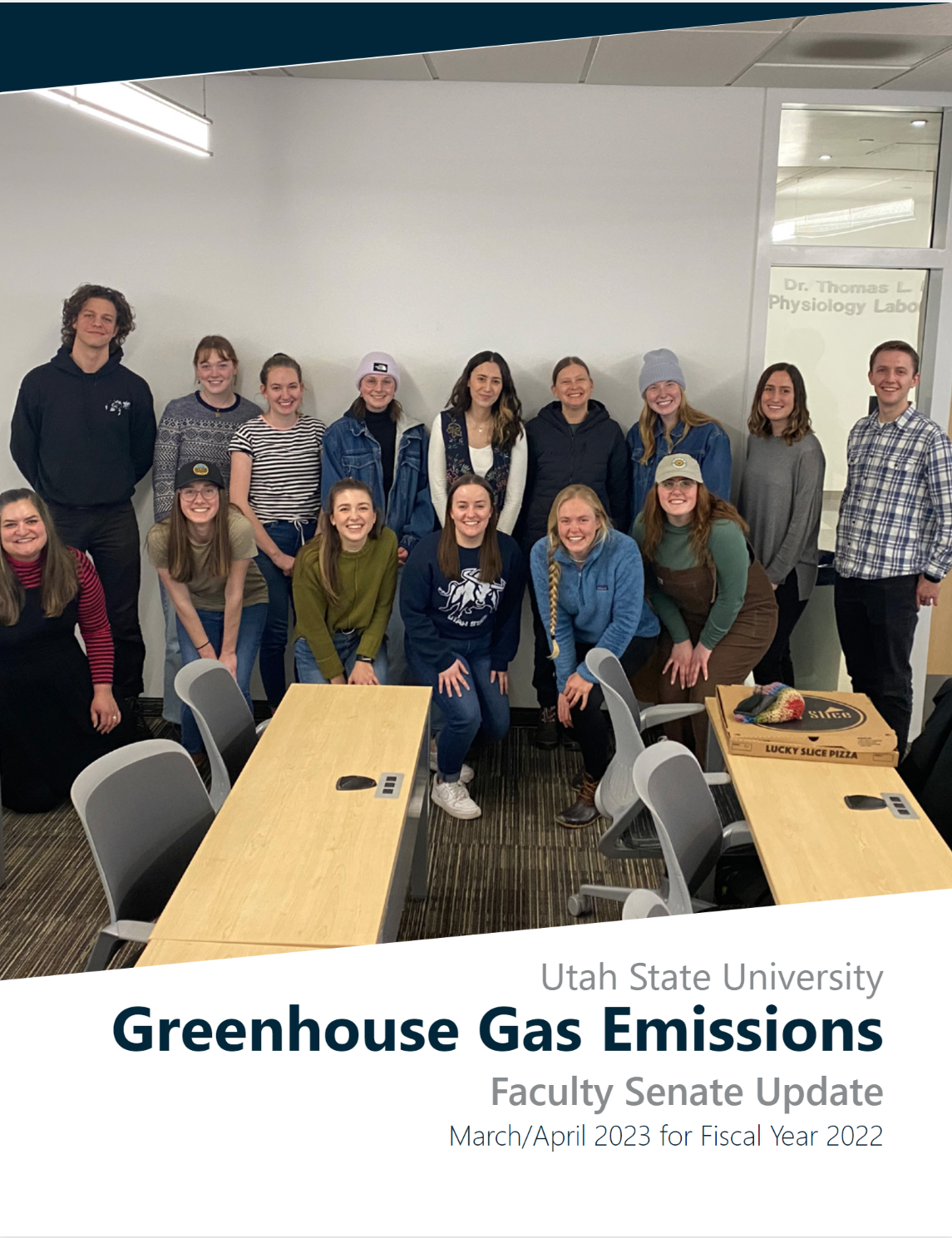 A group of staff and students look into the camera smiling in a classroom. The front of the image reads "Utah State University Greenhouse Gas Emissions; Faculty Senate Update"