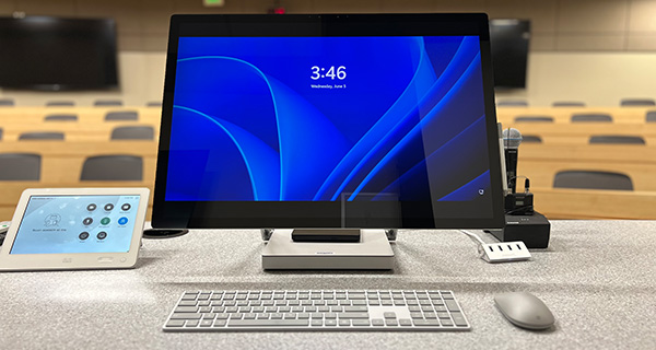 A computer sitting on a desk facing a classroom.