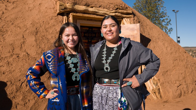Two native american students stand outside a Hogan