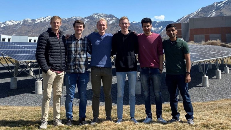 A group of students poses in front of a solar panel array.