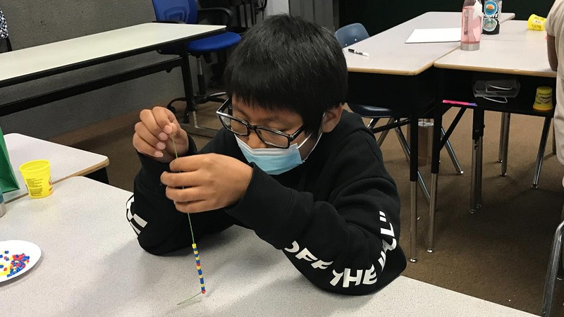 A student putting beads on a string.
