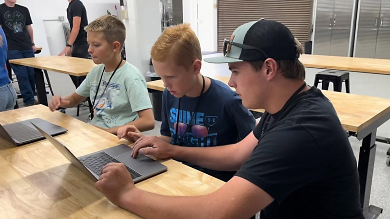 Three boys use laptops in a lab classroom.