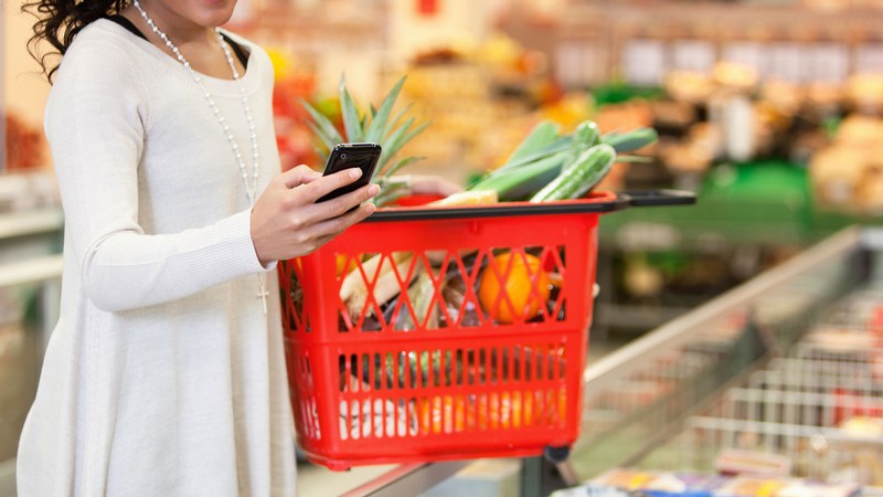 A person uses a smart phone while holding a grocery basket.