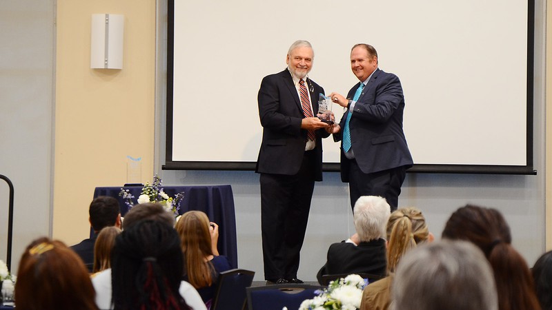 Two men standing on a stage holding an award.