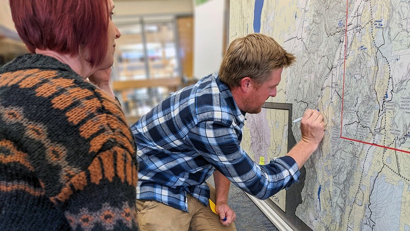 People kneeling as they draw on a large map of Utah wilderness.