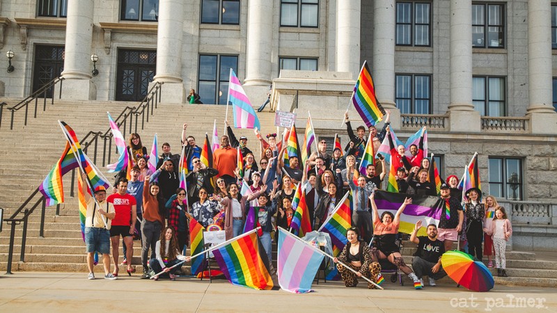 People hold Pride flags as they stand on the steps of the Utah Capitol.