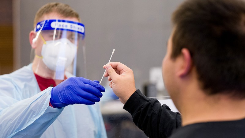 A health care worker in protective equipment hands a nasal swab to a person.