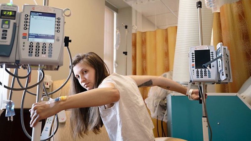 Sara Winston holding onto two intravenous drip machines in a hospital.