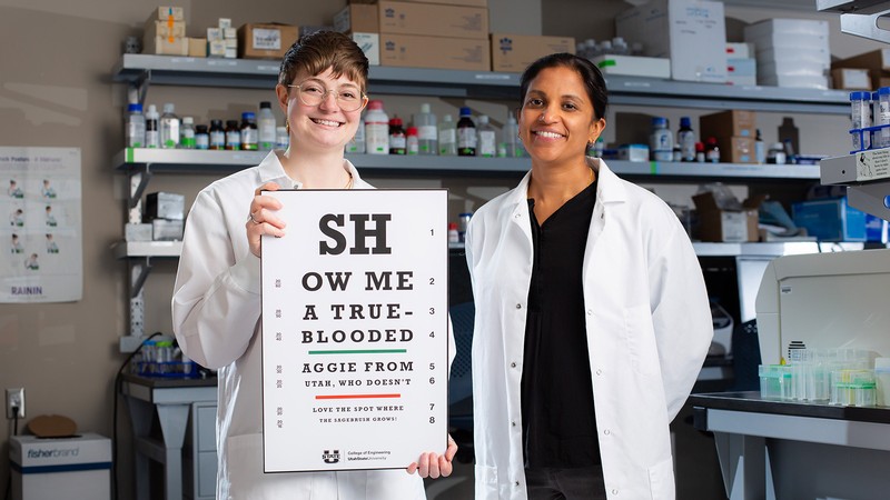 Researchers holding a vision test that shows lyrics from "The Scotsman" USU fight song.
