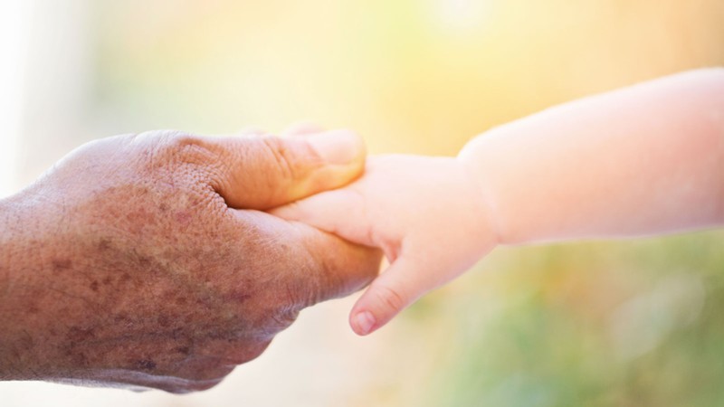 An older person's hand holding an infant's hand.