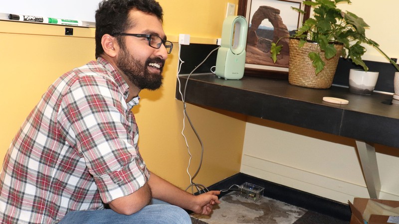 A scientist pointing to a small electronic device on the floor.