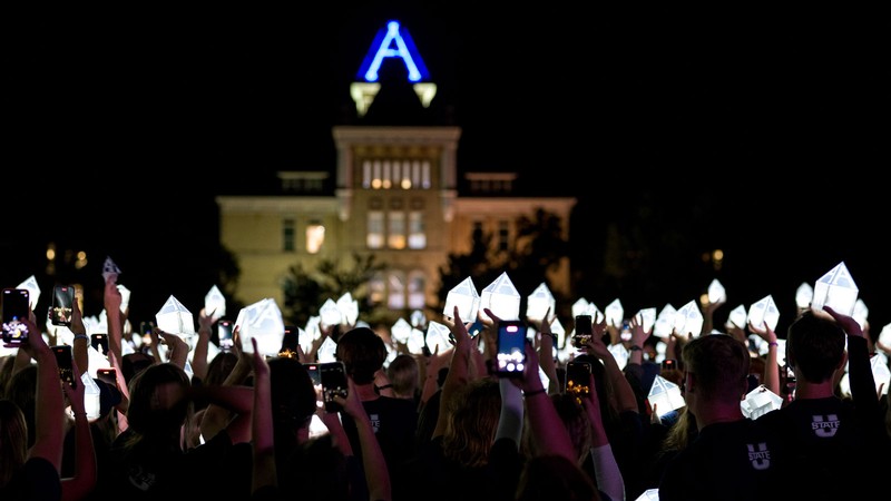 Students hold lanterns shaped like Old Main's tower in front of Old Main.