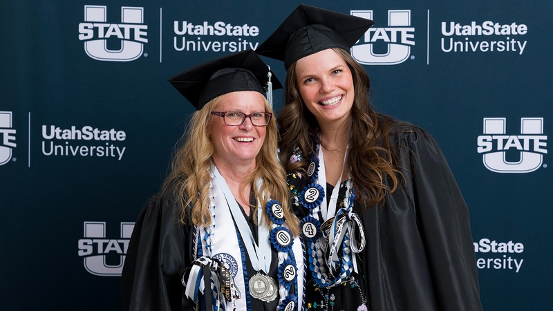 Two women stand together in graduation regalia.