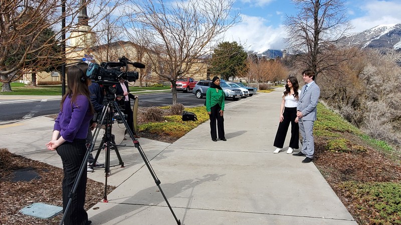 Students using a television camera to film a news segment.