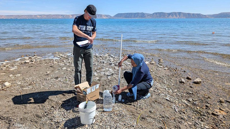 Brody Whiteaker and Thira Rahman collect samples on the shore of Bear Lake.