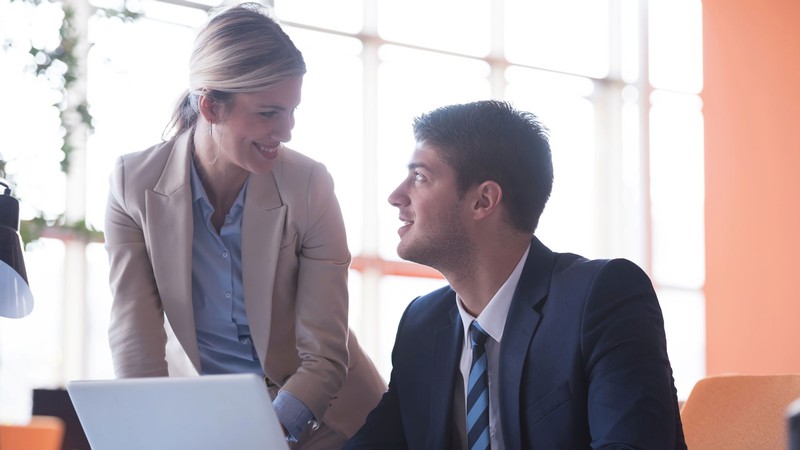 Two people smiling at each other in a workplace.