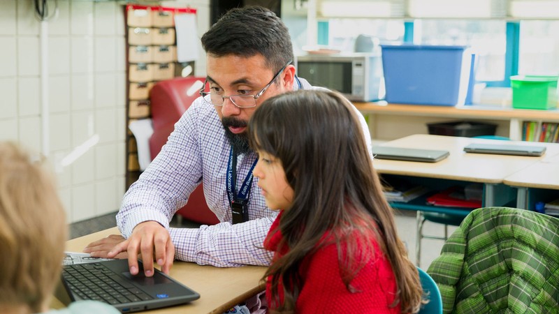 A teacher and a student using a laptop in a classroom.
