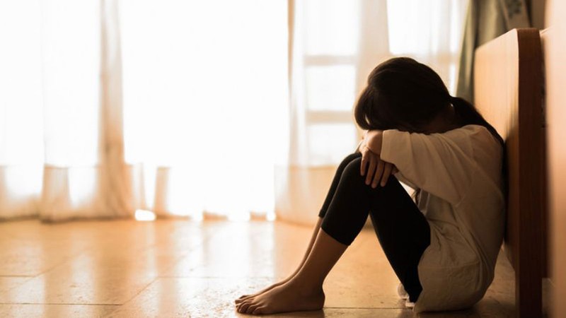 A woman sitting on the floor with her head on her forearms.