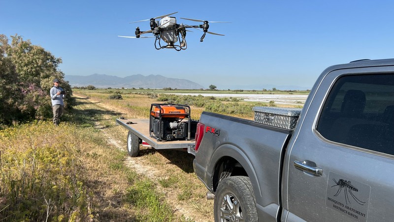 A pilot launching a drone from a trailer in a field.