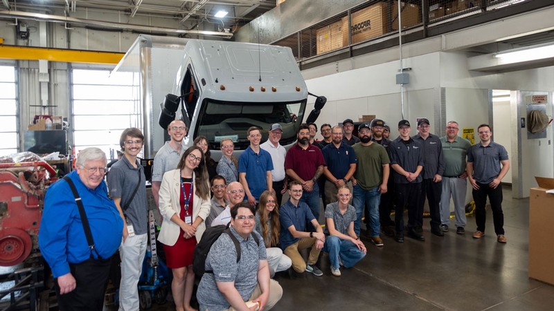 A group photo in front of a box truck in a mechanic's bay.