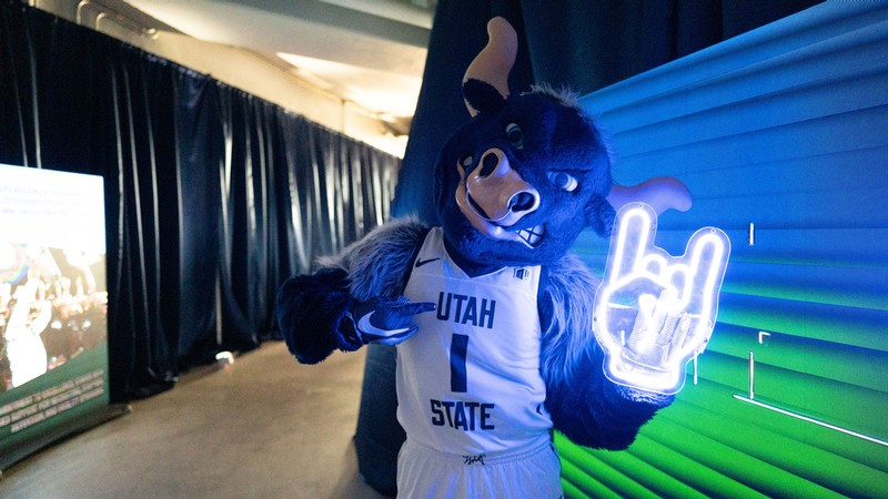 Utah State mascot Big Blue holding a neon sign of a hand making a bull horns sign.
