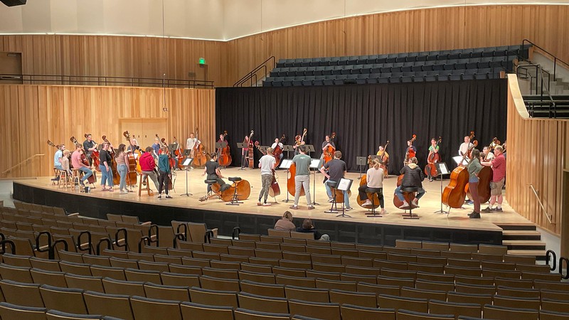 A group of students stand on a stage with string instruments