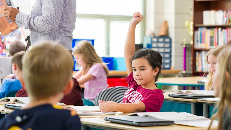 A child raises their hand in a classroom.