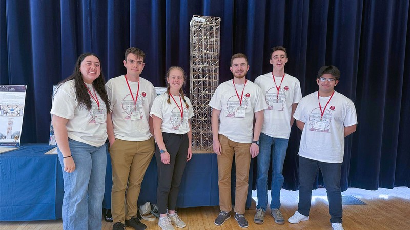 A group of students posing for a picture with a balsa model of a building.