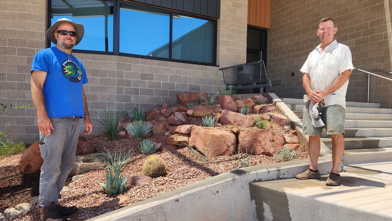 Two people standing by an area landscaped with red rock and desert plants.