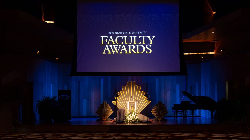 A stage. Text on a projector screen reads "2025 Utah State University Faculty Awards."