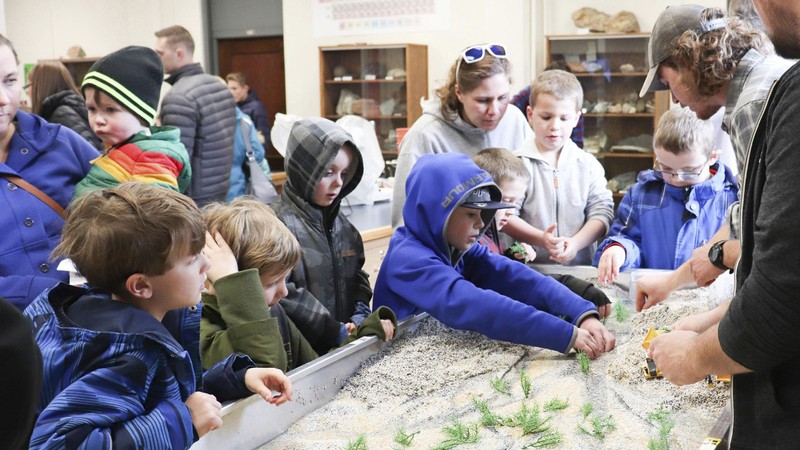 People interacting with a science exhibit in a sandbox.