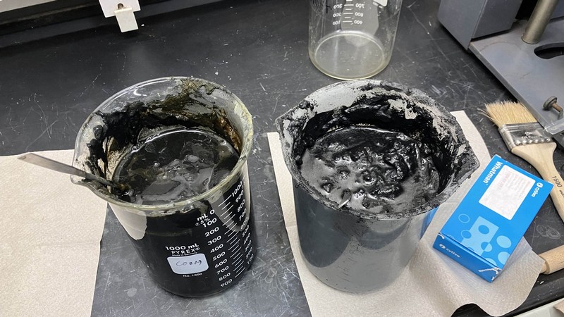 Beakers of a black, sticky substance in a lab.