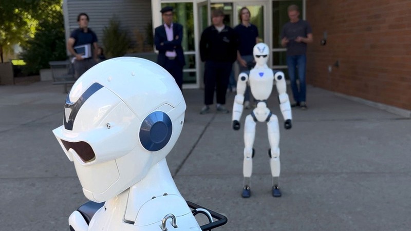 Engineers watching a demonstration of two humanoid robots.