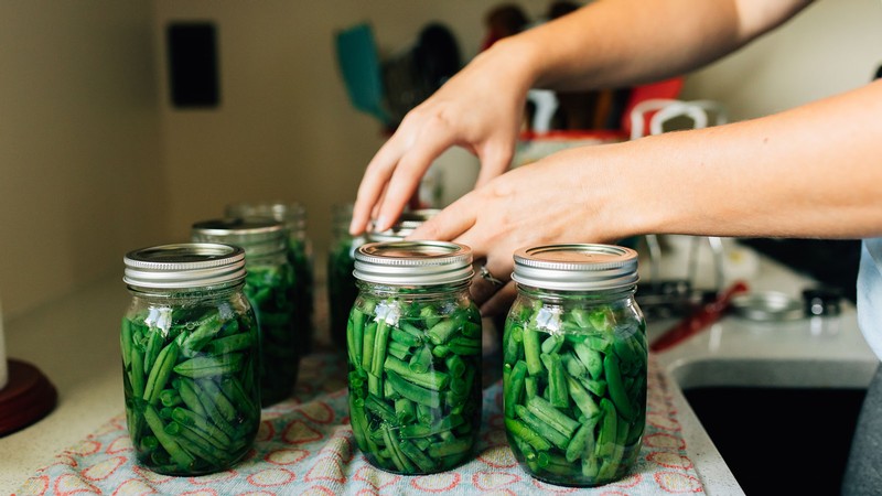 A person putting lid rings on jars of preserved green beans.