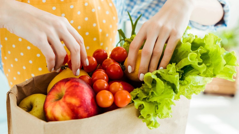 A person picking up fresh produce from a grocery bag.