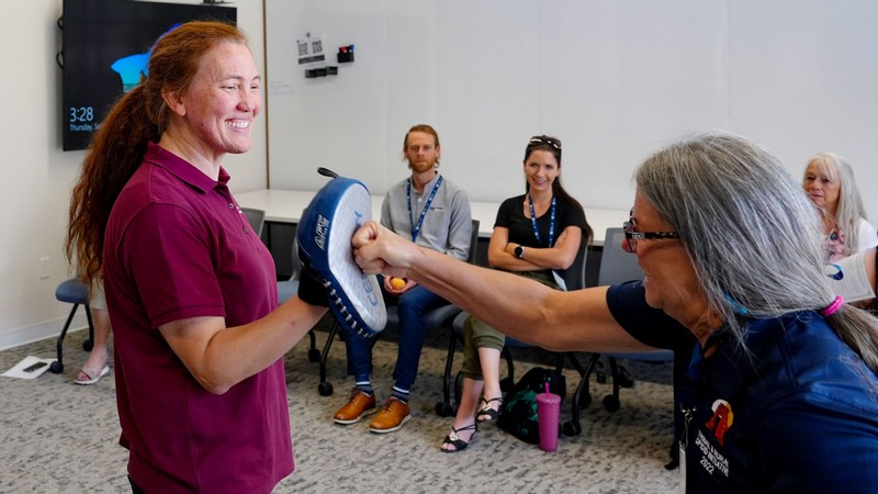 A woman punching a strike pad worn by an instructor.