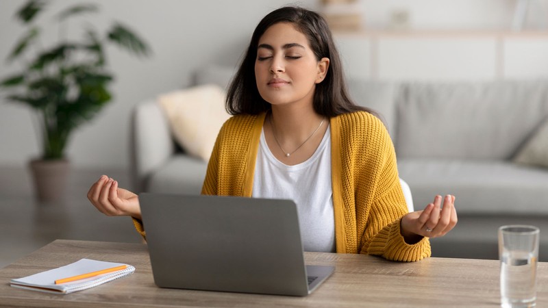 A person meditating by a laptop.