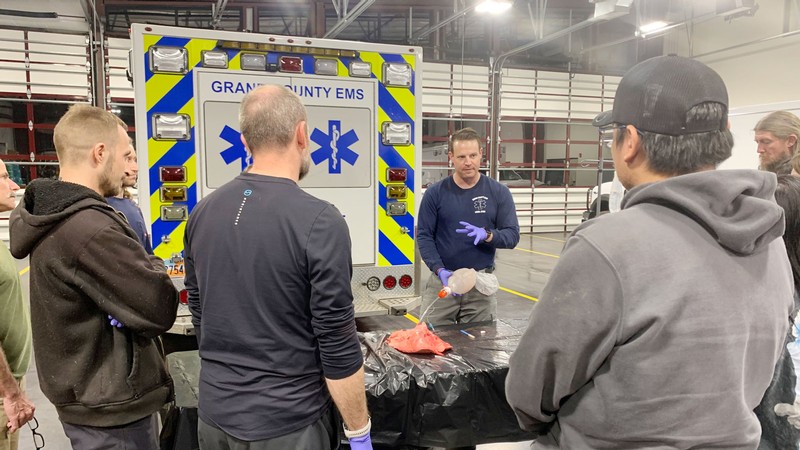 An instructor demonstrates EMT skills in an ambulance garage.