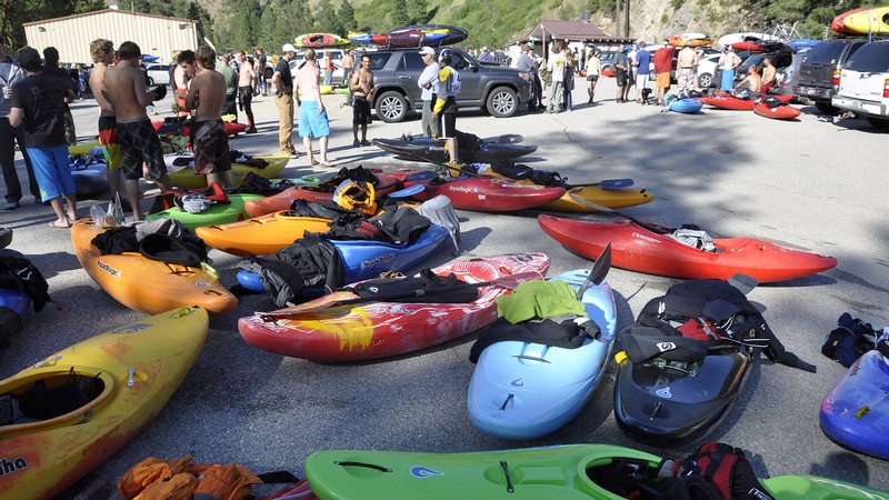 People talking near kayaks laid in a parking lot.