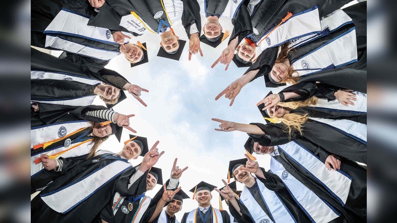 Students posing in a circle and wearing graduation robes make bull horn hand signs.