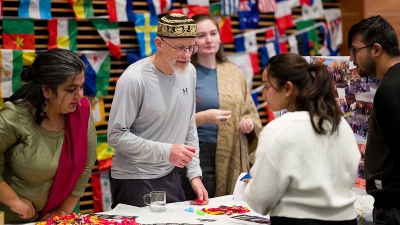 People speaking at an informational table in front of international flags.