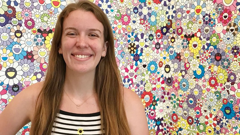 Julie Petersen poses for a photograph in front of a backdrop of colorful, smiling cartoon flowers.