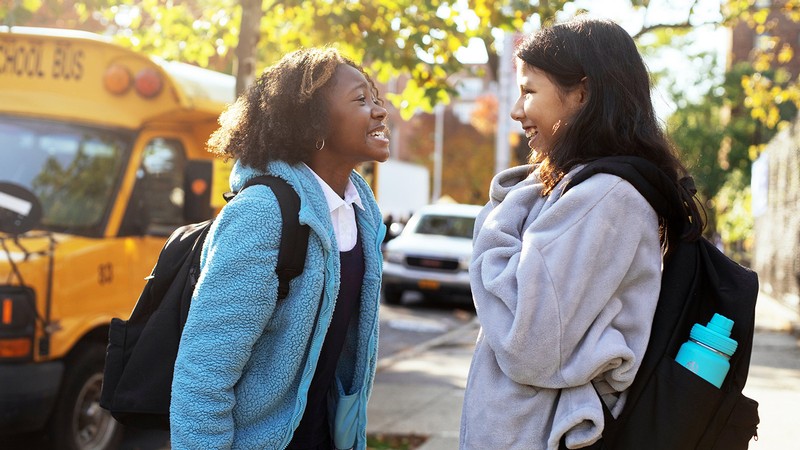 Two adolescent students chatting after getting off the bus.
