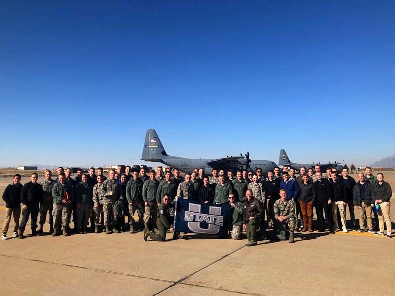 USU Air Force ROTC cadets pose with USU flag in front of a C-130 cargo plane.