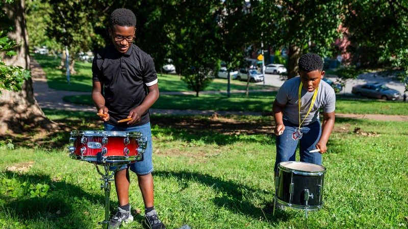 Two children playing drums outside.