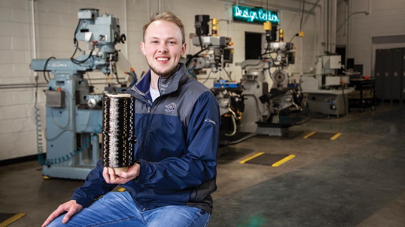Elijah Kimmel poses with a spool of material in a USU manufacturing lab.