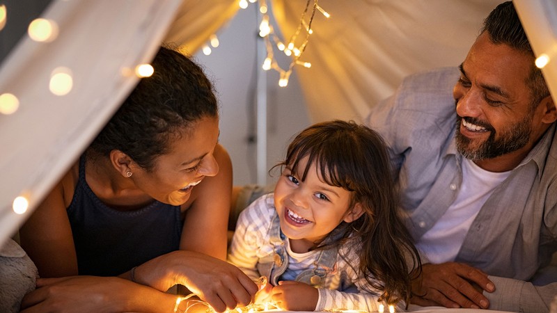 Mother and father snuggle in a tent with their daughter.