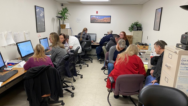 Multiple people sit around desks looking at computers and tax returns.